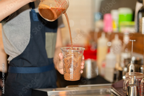 Barista pouring iced chocolate into takeaway cup in cafe.