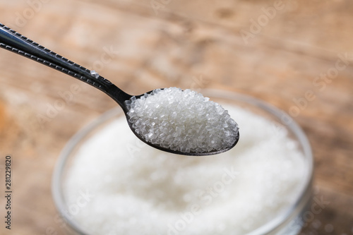 Sugar being poured from spoon into a bowl.  Bowl of sugar with spoon on wooden table