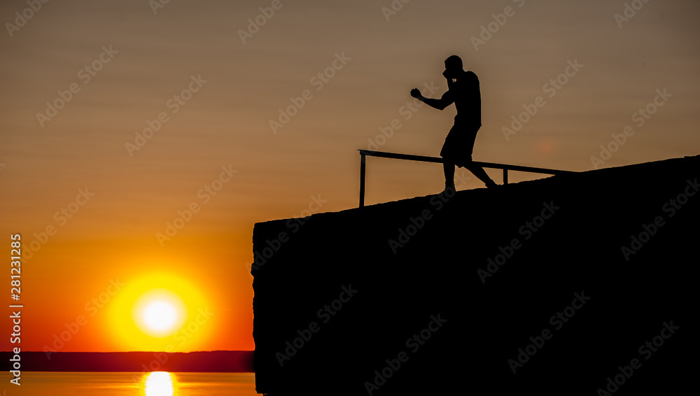 Silhouette of Young Strong Male Boxer Working Out On The Pier