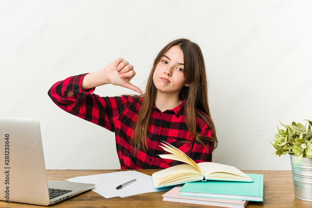 Young teenager going back to her routine doing homeworks showing a dislike gesture, thumbs down. Disagreement concept. Young teenager going back to her routine doing homeworks showing a dislike gesture, thumbs down. Disagreement concept.