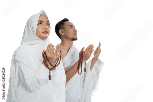 Muslim man and woman praying while standing in white traditional clothes ihram isolated over white background photo