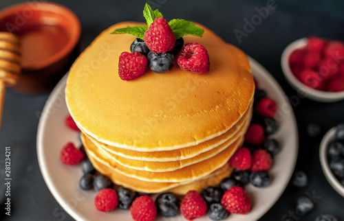 American pancakes with raspberries, fresh blueberries and honey. Healthy morning breakfast on concrete background