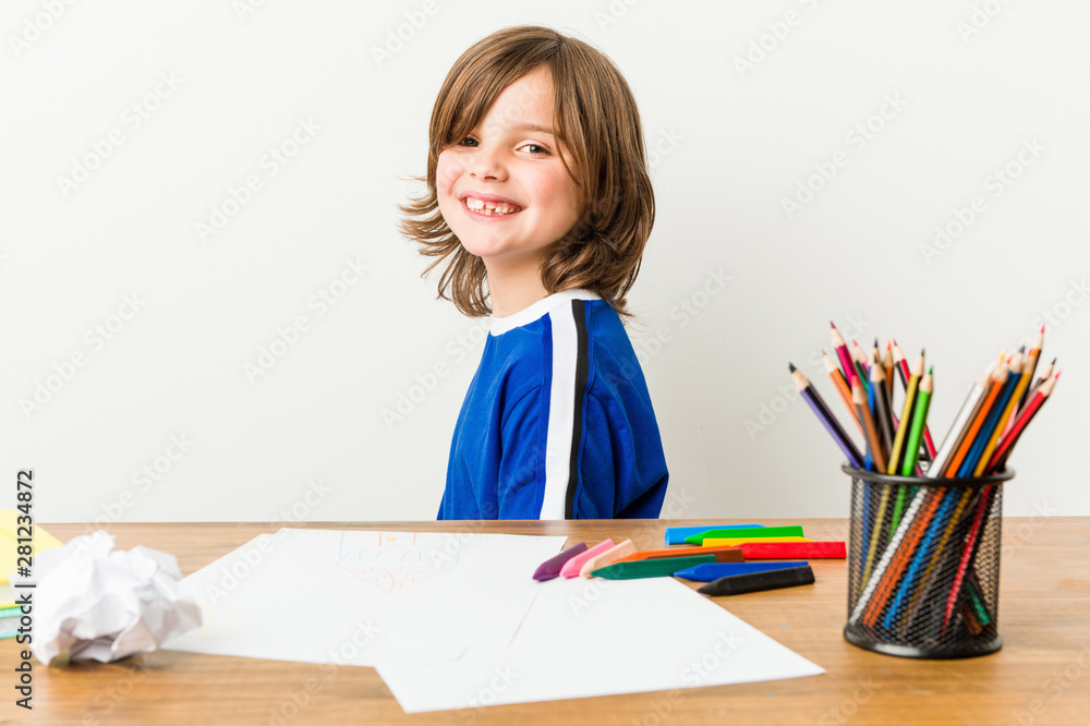 Little boy painting and doing homeworks on his desk looks aside smiling, cheerful and pleasant. Little boy painting and doing homeworks on his desk looks aside smiling, cheerful and pleasant.