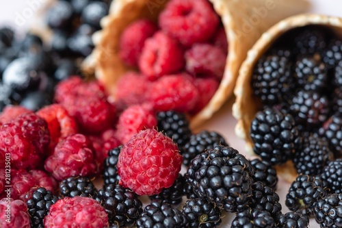 Raspberries, currants, blackberries closeup poured out of waffle cones, the focus is on raspberries