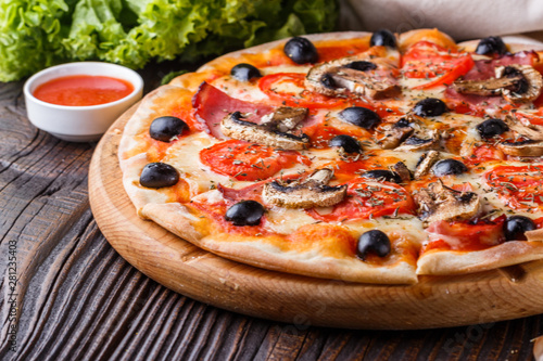 Pizza with tomato, olives, champignons, ham and cheese on round wooden plate
