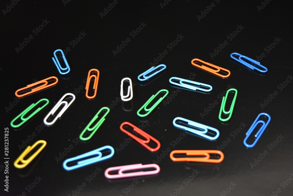 Many bright glossy colorful paper clips lie on a black glossy surface with reflection. Many bright glossy colorful paper clips lie on a black glossy surface with reflection.