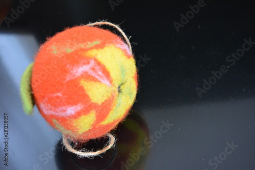 Soft Ukrainian toy made of natural wool and knocked down felt in the form of a bright ripe apple with a cheerful worm located on a black matte surface with reflection.