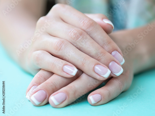 Closeup female french manicure in a beauty salon. Beauty woman nails on a mint background