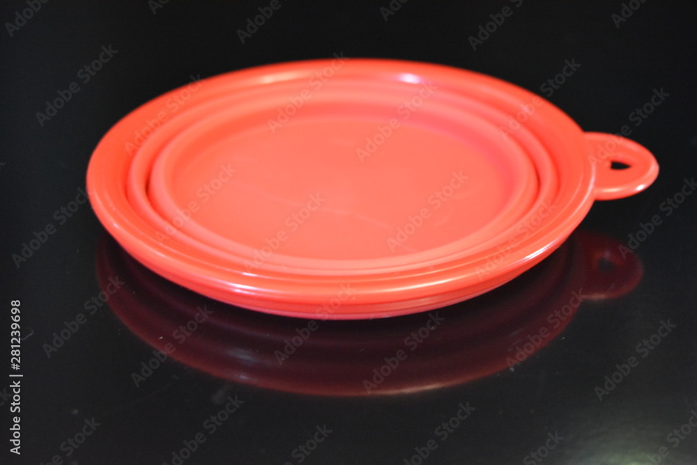 Red folding and multifunctional rubber plate, a bowl with a plastic edging on a black glossy surface. Red folding and multifunctional rubber plate, a bowl with a plastic edging on a black glossy surface.