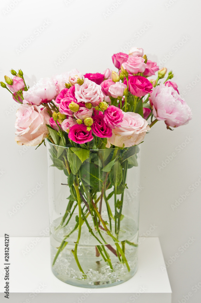 Bouquet of pink roses, peony flowers in glass vase on a shelf against white wall background. Bouquet of pink roses, peony flowers in glass vase on a shelf against white wall background.