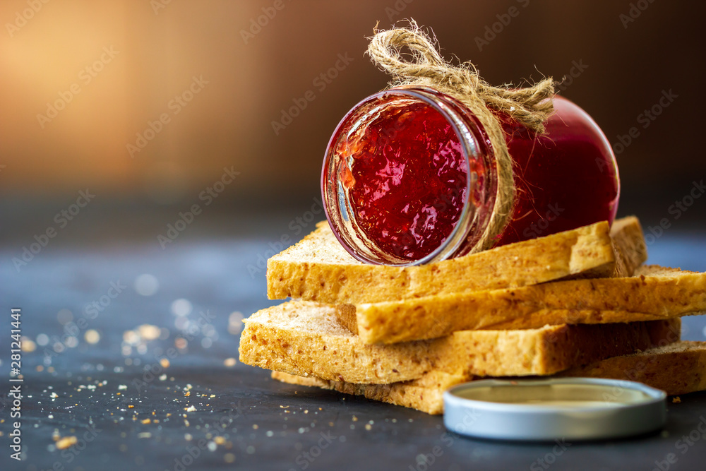 Strawberry jam bottle and whole wheat bread are stacked on a black background. Concept of breakfast and healthy food.