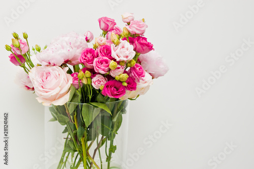 Fototapeta Naklejka Na Ścianę i Meble -  Bouquet of pink roses, peony flowers in glass vase on a shelf against white wall background.
