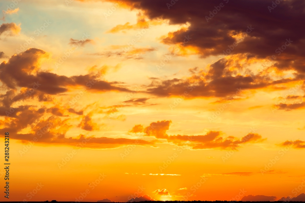 Fototapeta premium Beautiful bright majestic dramatic evening sky at sunset orange color with rays. The sun shines over the horizon against the backdrop of thunderclouds at dusk