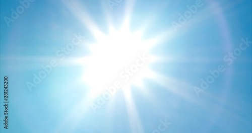 Looking up at bright, vivid sun with sunbeams and lens flare on blue summer sky