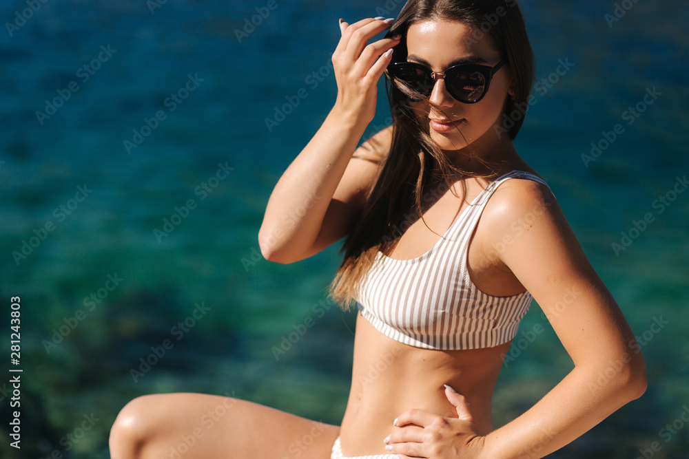 Portrait of sexy woman in front of turquoise lagoon. Beautiful color of the sea. Fathion model in bikini enjoing sun Portrait of sexy woman in front of turquoise lagoon. Beautiful color of the sea. Fathion model in bikini enjoing sun