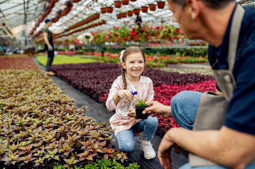 Happy little girl watering plants with her father in a greenhouse.