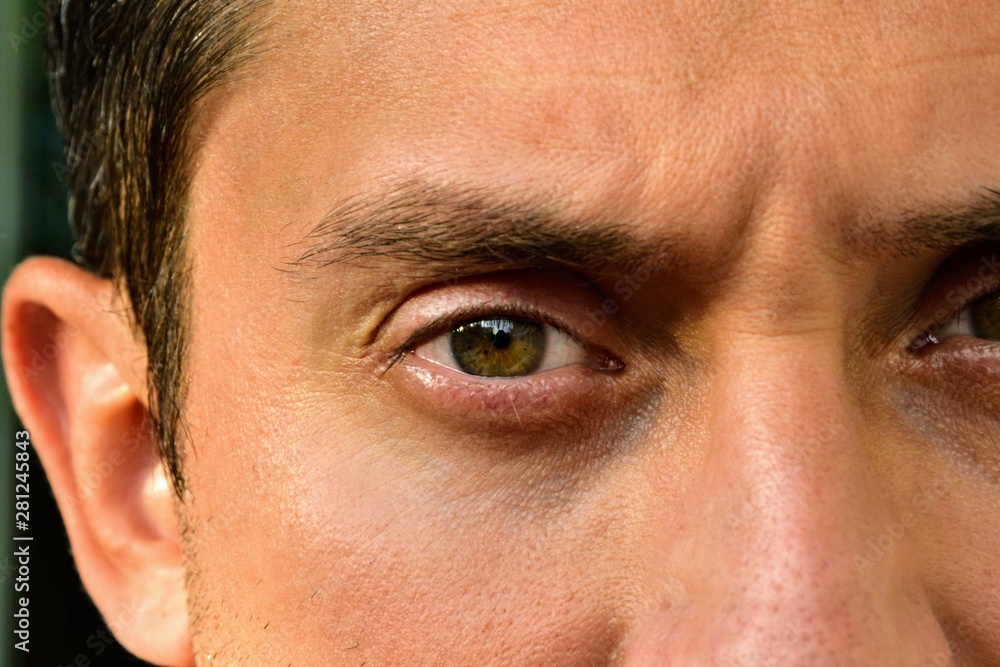 Fototapeta premium Detail of a brown eye of a handsome man looking at camera. Details of a male face, closeup. Looking angry man