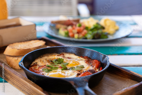 Side view of shakshuka with tomatoes, salami, chili pepper and fried eggs, served in hot cast pan