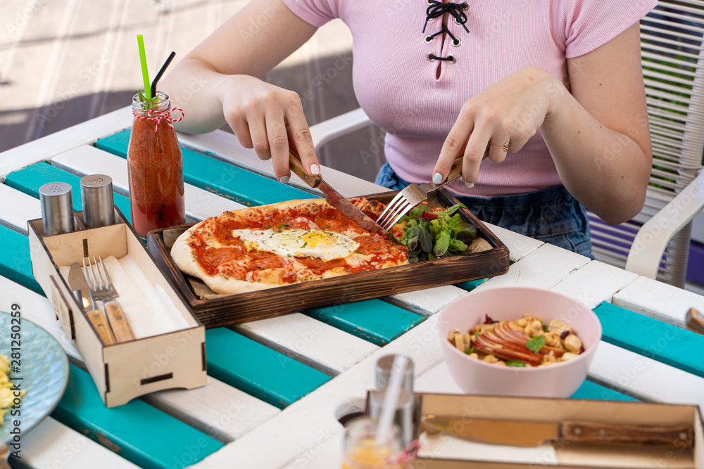 Woman is eating rome pizza with pepperoni, tomatoes and fried egg on a summer terrace Woman is eating rome pizza with pepperoni, tomatoes and fried egg on a summer terrace