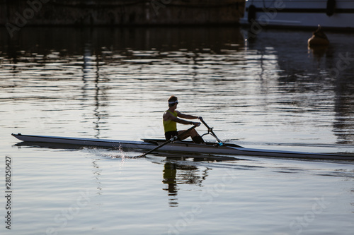 A man in a yellow shirt kayaking in a port near yachts and boats at dawn. Summer travel kayaking. Man paddling canoe. Exploring sea on vacation.