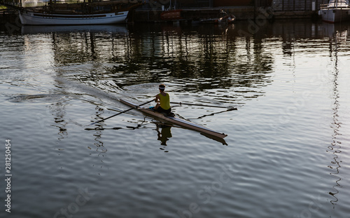 A man in a yellow shirt kayaking in a port near yachts and boats at dawn. Summer travel kayaking. Man paddling canoe. Exploring sea on vacation.