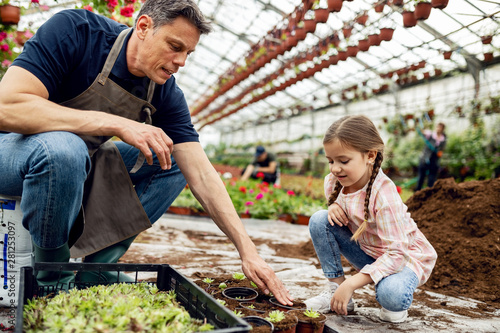 Father and daughter planting flowers together in a greenhouse.