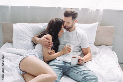 attractive and brunette woman and man lying on bed and hugging