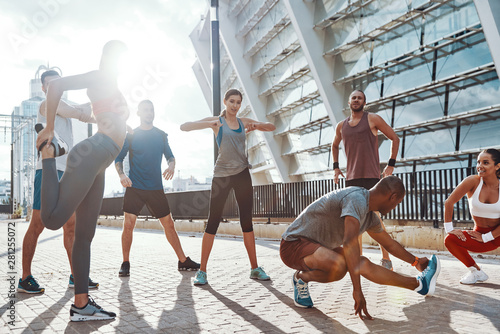 Full length of people in sports clothing warming up and stretching while exercising on the sidewalk outdoors