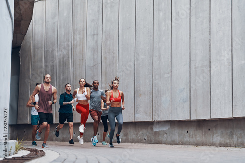 Fototapeta Naklejka Na Ścianę i Meble -  Full length of young people in sports clothing jogging while exercising outdoors
