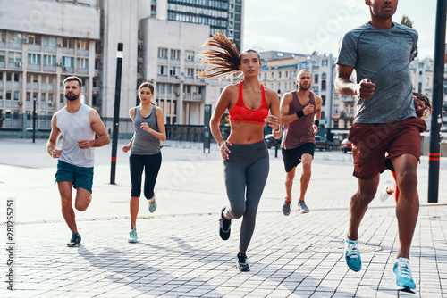 Fototapeta Naklejka Na Ścianę i Meble -  Group of people in sports clothing jogging while exercising on the sidewalk outdoors