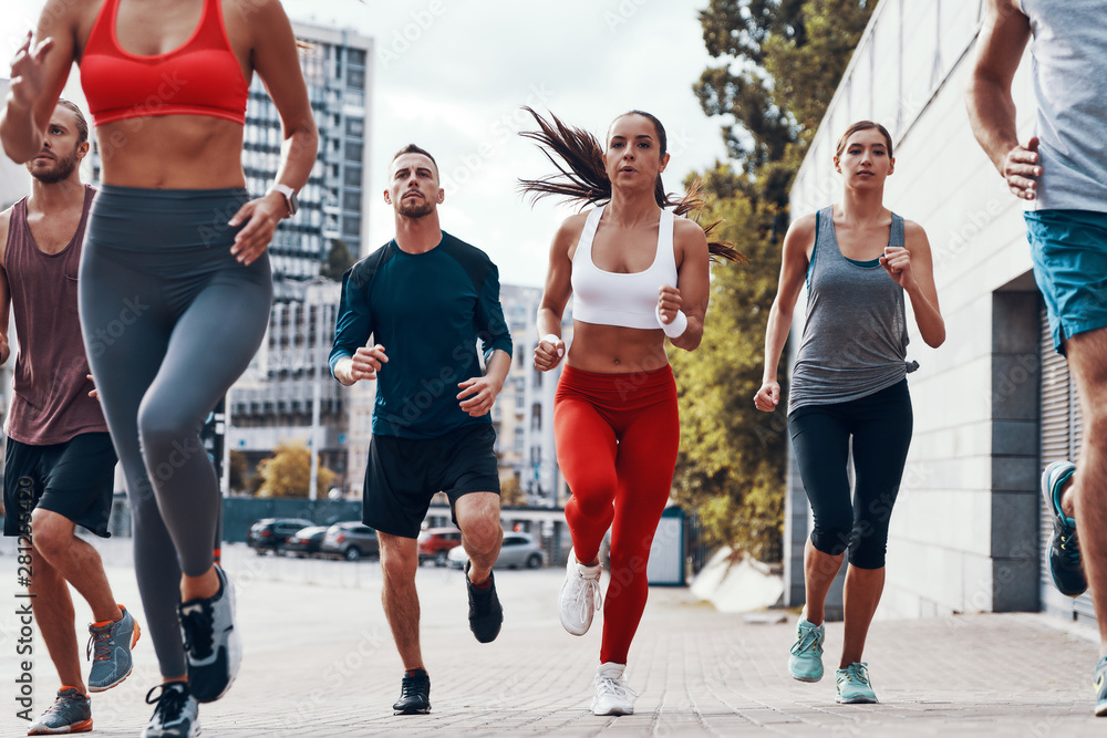 Fototapeta premium Group of young people in sports clothing jogging while exercising on the sidewalk outdoors