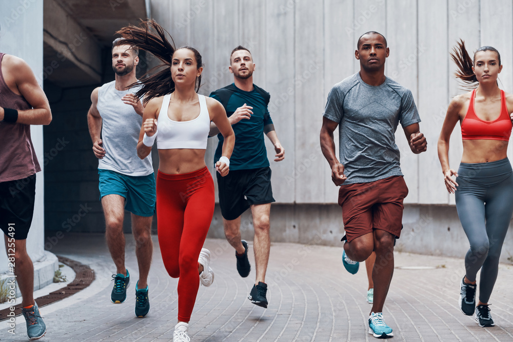Group of young people in sports clothing jogging while exercising outdoors
