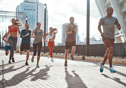 Fototapeta Naklejka Na Ścianę i Meble -  Full length of people in sports clothing jogging while exercising on the sidewalk outdoors
