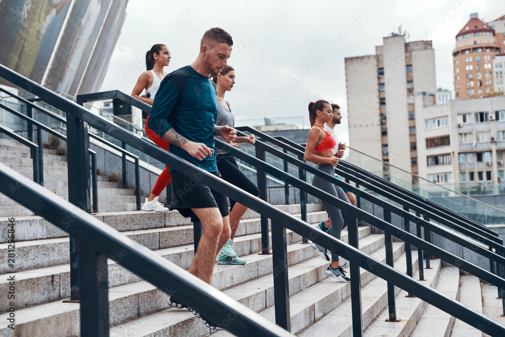 Group of young people in sports clothing jogging while exercising on the stairs outdoors