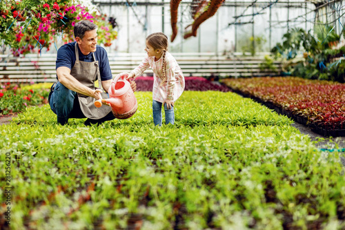 Billede på lærred Happy father and daughter talking while watering flowers at plant nursery
