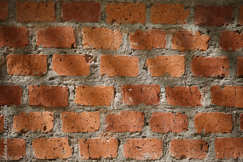 Fototapeta premium The falling rays of the sun on the old red brick wall. Texture of a rough weathered brick wall