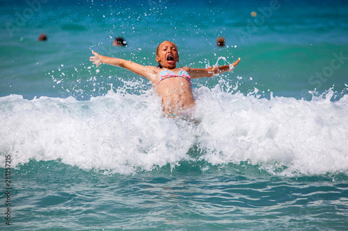 Young girl laughing and crying in the spray of waves at sea on a sunny day..