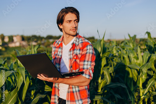 Agronomist standing in a field holding open  laptop and smiling and looking out-Image