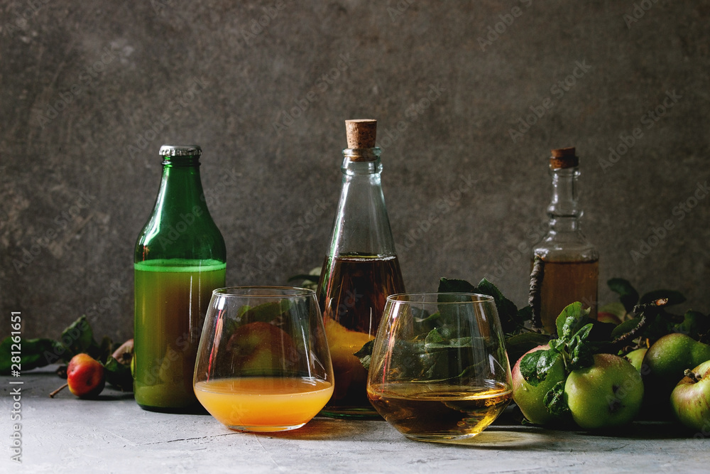 Variety of apple drinks. Bottles ang glasses of apple juice, vinegar and cider with garden apples with leaves and branches on table with dark background. Autumn home harvesting. Variety of apple drinks. Bottles ang glasses of apple juice, vinegar and cider with garden apples with leaves and branches on table with dark background. Autumn home harvesting.