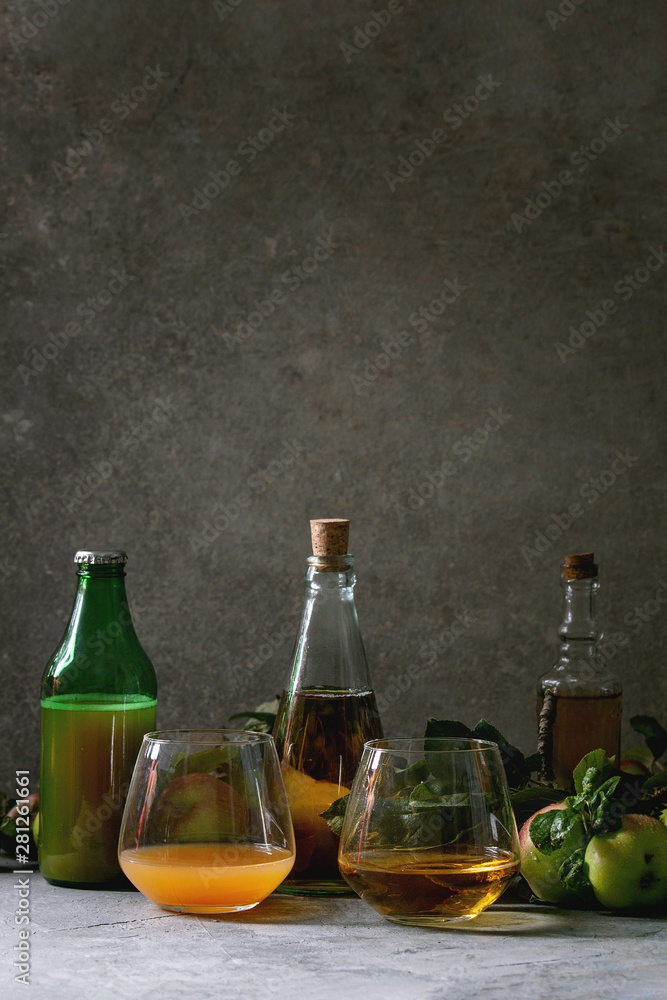 Variety of apple drinks. Bottles ang glasses of apple juice, vinegar and cider with garden apples with leaves and branches on table with dark background. Autumn home harvesting. Variety of apple drinks. Bottles ang glasses of apple juice, vinegar and cider with garden apples with leaves and branches on table with dark background. Autumn home harvesting.