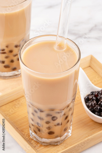 Tapioca pearl ball bubble milk tea, popular Taiwan drink, in drinking glass with straw on marble white table and wooden tray, close up, copy space.