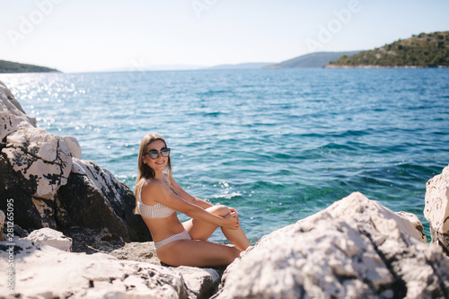 Sexy woman in sunbathing and enjoying summer sun on the rock. Woman on sea background. Relax on vocation