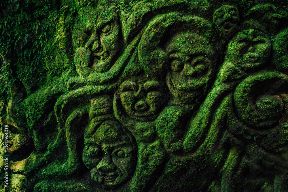 Carving demons faces on wall background covered with moss texture in ...