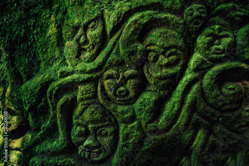 Carving demons faces on wall background covered with moss texture in Bali