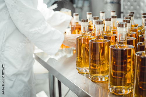 Small liquor production based on maple syrup. Lot of pure alcohol bottles unlabeled. Bottles placed in a row. Person in lab coat analyzing the bottles.