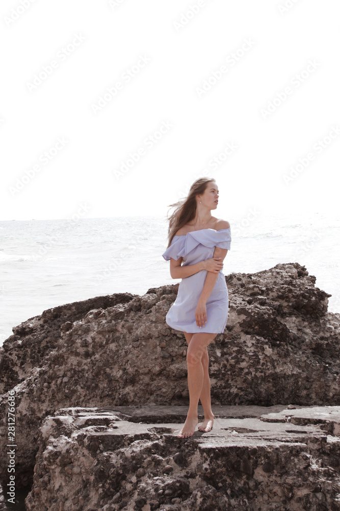 Young caucasian woman in blue summer dress stay on the rocks Young caucasian woman in blue summer dress stay on the rocks