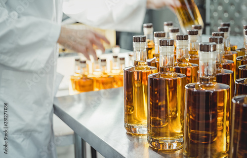 Small liquor production based on maple syrup. Lot of pure alcohol bottles unlabeled. Bottles placed in a row. Person in lab coat analyzing the bottles.