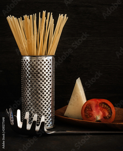 SPAGHETTI ON METAL TRAY WITH TOMATO, CHEESE AND METAL GRATER ON DARK FUND photo