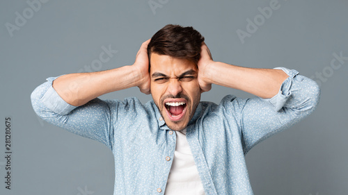 Emotional Hispanic Man Screaming Covering His Ears On Gray Background