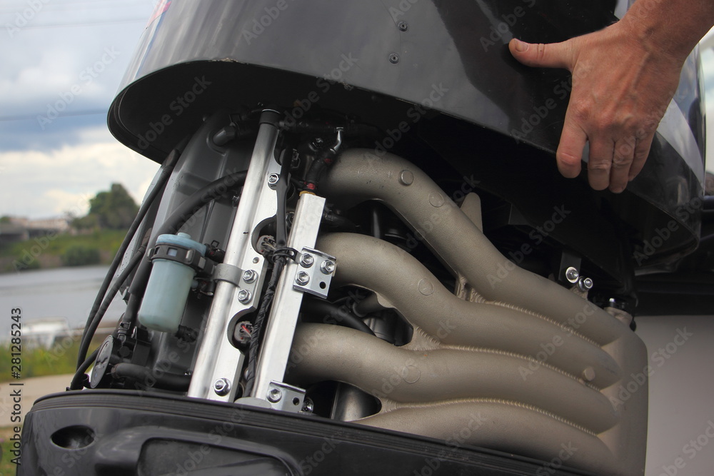 A man's hand closes the hood of a powerful outboard boat motor, repair and maintenance of boat engines, a view of the intake manifold of a four-cylinder four-stroke injector motor